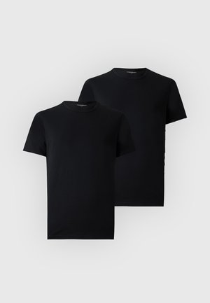 Homme debout pieds nus portant un t-shirt noir moulant à manches courtes et un short moulant couleur rouille sur un fond clair uni.