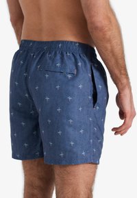 Blauwe zwemshorts van lichtgewicht stof, met een subtiel palmbomenpatroon, elastische tailleband en een achterzak met klep.