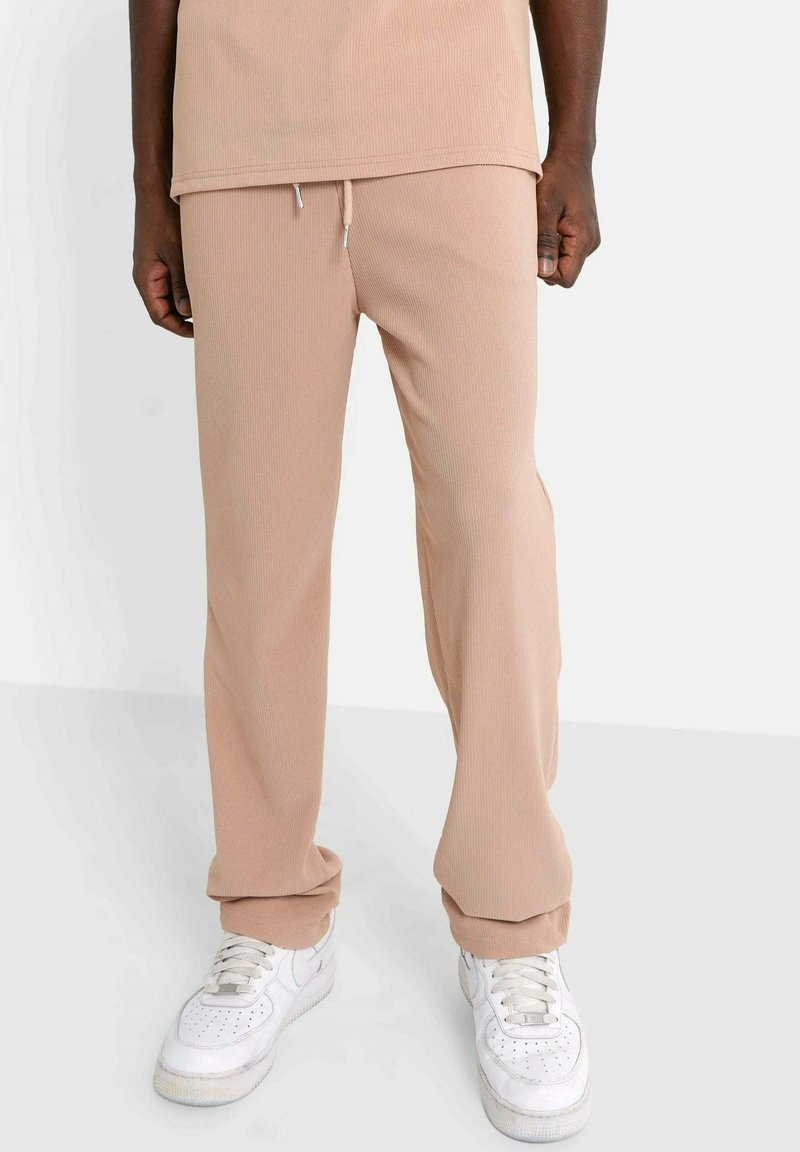Beige geribde sweatpants met een elastische tailleband, contrasterend trekkoord en taps toelopende boorden. Gepaard met witte sneakers.