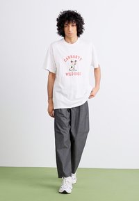 White oversized t-shirt with red "Carhartt Wild Dogs" graphic; paired with loose charcoal pants and white sneakers.