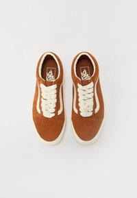 Baskets en suede marron avec des accents et des lacets blancs, arborant un design bas et une finition texturée. Logo imprimé sur la languette.