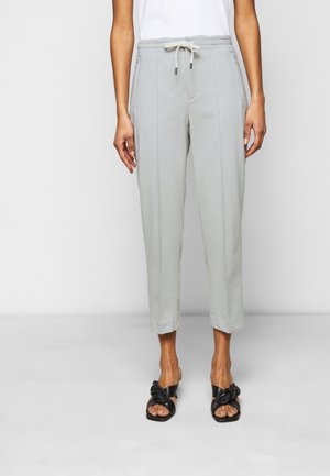 Kobieta nosząca jasnoszare spodnie do kostek ze ściągaczem w talii i czarne sandały na obcasie z plecionymi paskami.