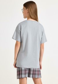 Grå bomulds t-shirt med korte ærmer, parret med en plisseret ternet nederdel i grå, burgunder og sorte nuancer. Blød tekstur, afslappet pasform.