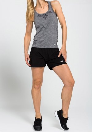 Harso urheilullinen tankki, jossa on verkkomaisia yksityiskohtia, yhdistettynä mustiin shortseihin. Mallilla on päällään mustat lenkkarit. Tausta on yksinkertainen valkoinen.