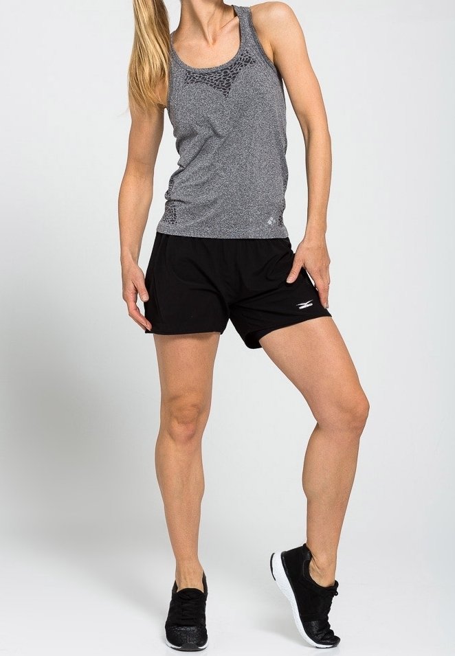 Top deportivo gris con detalles de malla, combinado con pantalones cortos negros. El modelo lleva zapatillas negras. El fondo es blanco liso.