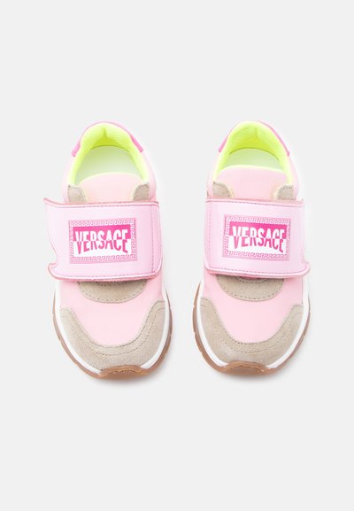 Ζευγάρι ροζ παιδικά αθλητικά παπούτσια με μπεζ σουέτ λεπτομέρειες και φαρδιές ροζ λουράκια Velcro με την επωνυμία "VERSACE" σε λευκό φόντο.