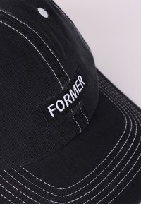 Șapcă neagră cu o coamă curbată, cusături albe și un patch brodat cu textul "FORMER". Fabrică din bumbac texturat cu o coroană domedă.