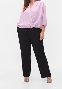 Blusa di un leggero viola con scollatura a V e maniche a palloncino, abbinata a pantaloni neri. Le calzature presentano un design con cinturini decorati.