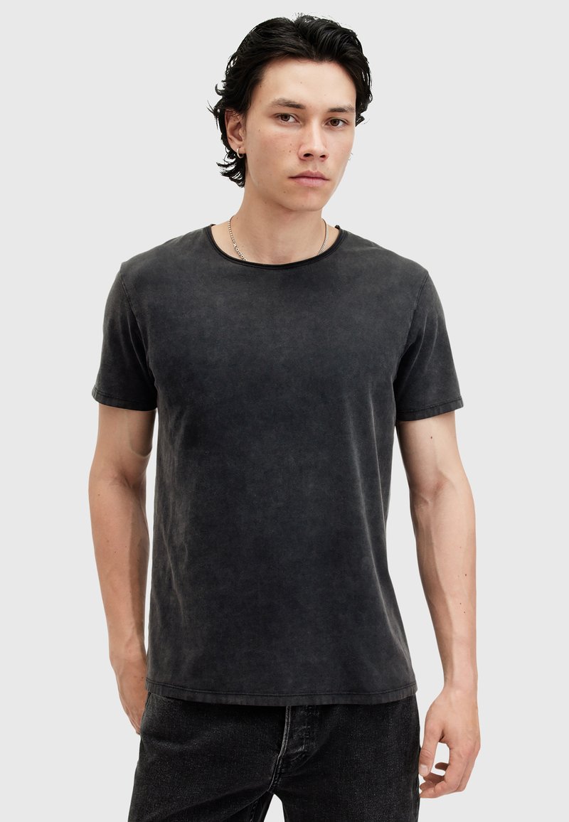 Schwarzes Rundhals-T-Shirt aus weichem Stoff mit einem verblassten Textur. Kurze Ärmel und eine lockere Passform, kombiniert mit dunklen Jeans.