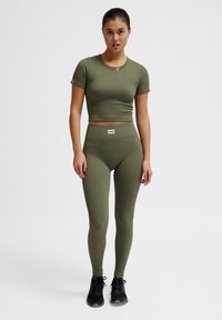 Olivgroene geribbelde cropped top en hoge taille legging, gemaakt van elastisch materiaal, gecombineerd met zwarte sportschoenen. Minimalistisch logodetail.