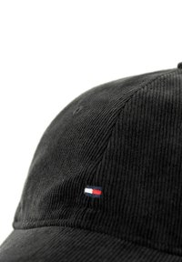 Gorra de béisbol de corduroy negro con un pequeño logo bordado en colores rojo, blanco y azul en el lateral, destacando textura y forma.