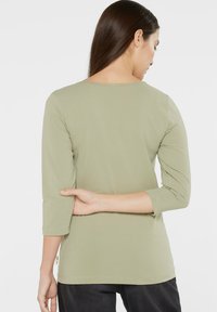 Olive green, three-quarter sleeve top with round neckline, soft texture, back view showing subtle stitching and hem detail.
