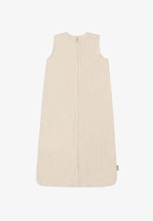 Sac de couchage en coton beige clair avec fermeture éclair, design sans manches et surface texturée. Présente une petite étiquette logo sur le côté.