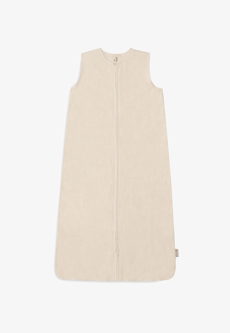 Sac de couchage en coton beige clair avec fermeture éclair, design sans manches et surface texturée. Présente une petite étiquette logo sur le côté.