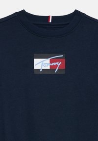 Marineblaues Sweatshirt mit geripptem Rundhalsausschnitt, das ein farbblockiertes Logo-Patch in Schwarz, Weiß, Rot und Blau mit "Tommy" in hellblauer Schrift zeigt.