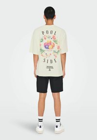 Camiseta blanca de manga corta con un gráfico de un tazón de bolas de billar de colores. El texto dice "POOL SIDE" en negro con acentos florales.