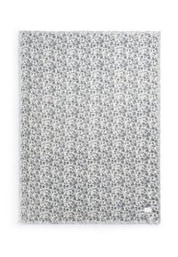 Blomstermønstret tæppe i creme og blå, med frynser i kanten og blødt, tekstureret stof. Firkantet størrelse, med en mærketag i hjørnet.