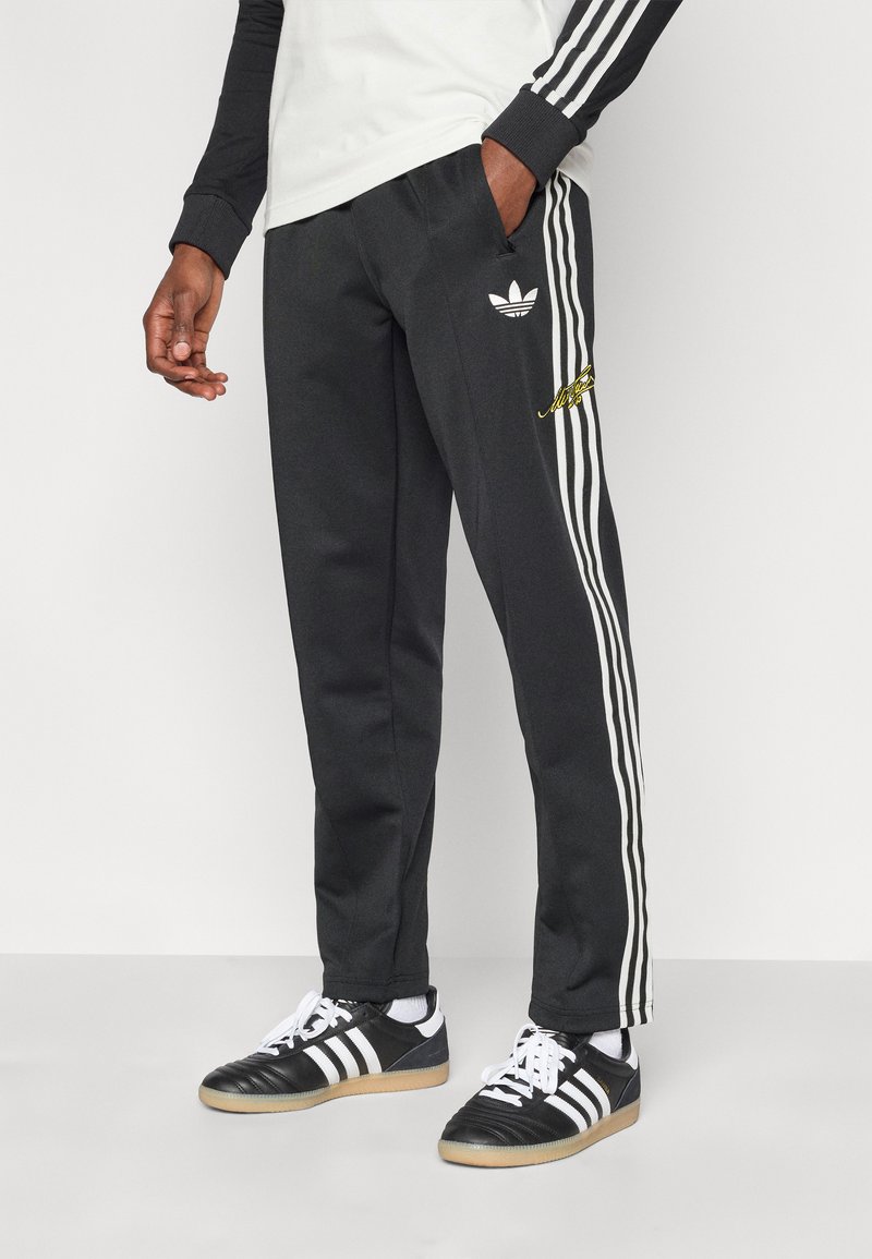 Μαύρο αθλητικό παντελόνι με λευκές ρίγες στα πλαϊνά, με μικρό λευκό λογότυπο και κίτρινες λεπτομέρειες, κατασκευασμένο από μαλακό ύφασμα με τσέπες.