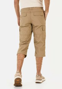 Beige cargo shorts med knælangt snit, flere sidelommer og struktureret talje. Båret med lyse sportsko.