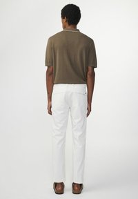 Brązowa koszulka polo z krótkim rękawem i białym kołnierzykiem, w połączeniu z dopasowanymi białymi spodniami i brązowymi sandałami, prezentująca czysty widok z tyłu.