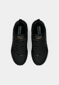 Czarne buty sportowe z fakturowaną cholewką z siateczki, tonowanymi sznurowadłami i miękką podeszwą. Charakteryzują się oznaczoną marką wkładką oraz lekkim połyskiem na czubkach.