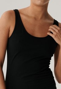 Czarna koszulka na ramiączkach z okrągłym dekoltem, bez rękawów, dopasowany krój oraz gładki materiał bawełniany, z delikatnym marszczeniem po bokach.
