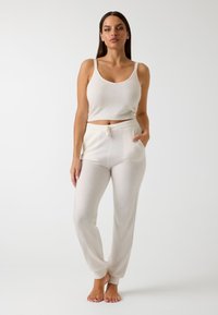 Balts, īss tank top, kas apvienots ar atbilstošām, brīvā piegriezuma biksēm ar elastīgu jostu un potītes aprocēm. Mīksta tekstūra ar minimālām detaļām.