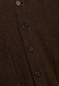 Cardigan marron tricoté avec une finition texturée, doté de cinq boutons noirs et de deux poches avant. Poignets côtelés et détails de la patte de boutonnage.