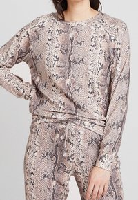 Długi rękaw, bluzka i pasujące spodnie w beżowo-brązowy wzór węża. Wykonane z miękkiego materiału, o luźnym kroju i elastycznym pasie z troczkiem.