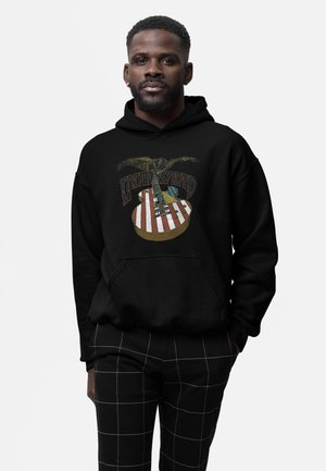 Haut à capuche noir avec un graphisme d'aigle et de guitare, avec des rayures rouges et blanches et des accents bleus. Associé à un pantalon à carreaux noir.