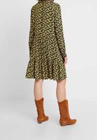 Svart blommig klänning med lång ärm, gult blommönster, volang nertill. Kombinerad med bruna mocka höga stövlar, med blockklackar.