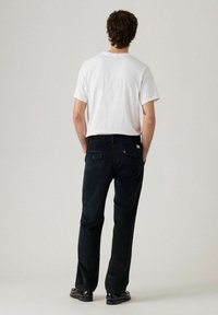 Pantaloni di velluto a coste a quadri scuri con design a gamba dritta, abbinati a una maglietta bianca semplice e calzature nere, visti da dietro.