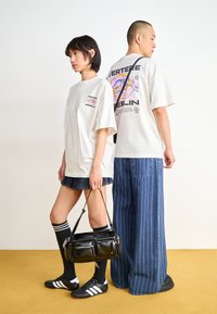 White oversized graphic t-shirts feature multicolored prints. The woman wears a denim skirt and black knee-high socks; the man has pinstriped pants.