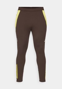 Pantalons de sport bruns avec poches latérales, dotés d'accents jaunes et de rayures verticales. Fabriqués en matériau flexible et respirant. Design ajusté.