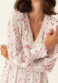 Blusa blanca con un estampado de hojas rojas y delicados bordados de encaje en el cuello y los puños. Mangas largas, tela ligera y fluida.