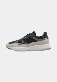 Athletic sneaker featuring a mix of black mesh and gray suede panels, green laces, and a thick white sole with a textured grip.