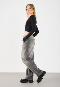 Črn rebrast dolgi rokav krojeni top, v kombinaciji s sproščenimi, zbledelimi sivo-modrimi kavbojkami in masivnimi črnimi platform čevlji. Preprost, sproščen dizajn obleka.