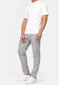 Weißes Baumwoll-T-Shirt kombiniert mit hellgrauen Slim-Fit-Hosen und weißen Sneakers. Glatte Textur ohne sichtbare Muster oder Logos.