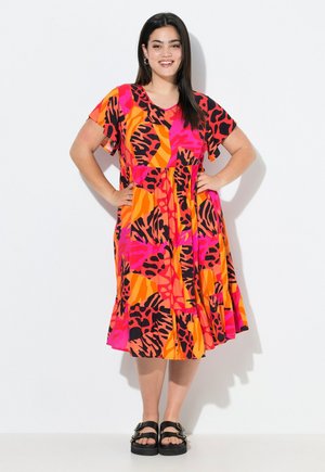 Kleurvolle jurk met korte mouwen en een uitlopende rok, versierd met gedurfde patronen in roze, oranje en zwart. Gemaakt met chunky zwarte sandalen.