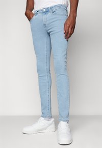 Vaqueros ajustados de color azul claro, confeccionados en denim, que presentan un diseño clásico de cinco bolsillos, detalles de costura y un cierre de botón. Combinados con zapatillas blancas.