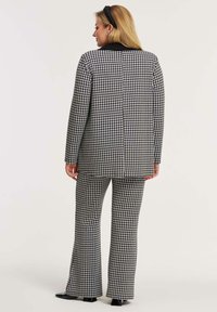 Sort-hvid houndstooth-sæt med en skræddersyet blazer og flagrende bukser, lavet af tekstureret stof med en glat finish.