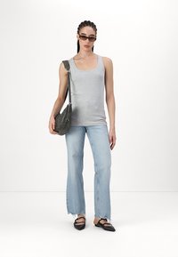 Graues Tanktop, hellblaue ausgestellte Jeans mit fransigen Säumen, schwarze Slipper und eine dunkelgraue Umhängetasche; trägt Sonnenbrille.
