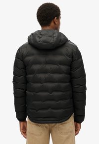 Czarna kurtka puchowa z kapturem, o pikowanej fakturze i elastycznych mankietach. Ma lekko dopasowany krój dla zapewnienia ciepła i komfortu.
