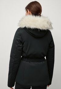 Sort jakke med en hætte foret med kunstpels, indsnøret talje og glat tekstur. Har elastiske detaljer og et praktisk design.