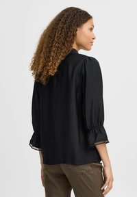 Blusa nera con una vestibilità rilassata, maniche leggermente a sbuffo e bordi in pizzo sui polsini. Tessuto morbido con una finitura opaca. Design semplice.