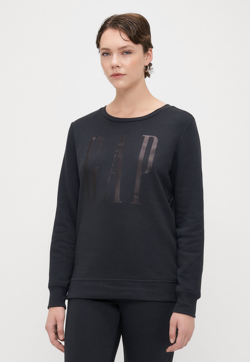 Sudadera negra de suave algodón con cuello redondo, con un logotipo brillante de "GAP" impreso en la parte frontal, mangas largas y puños acanalados.