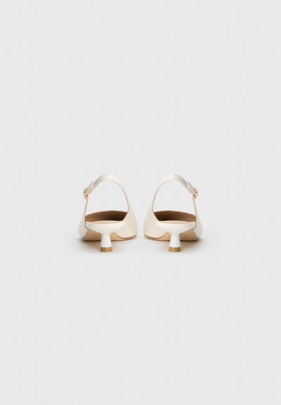 O pereche de pantofi slingback off-white cu toc jos, rotund și conic, și curele cu cataramă aurie, prezentată din spate pe un fundal alb simplu.
