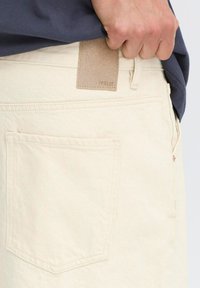 Shorts de mezclilla color crema con detalles de costura mínimos, que presentan una etiqueta de cuero en la cintura y un bolsillo trasero.