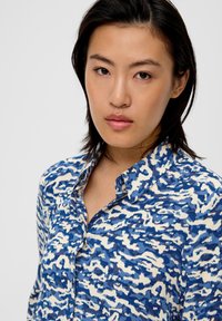 Hemd mit blau-weißer Musterung, ausgestattet mit einem Button-Down-Kragen, leicht strukturiertem Stoff und einem lässigen Schnitt. Nahaufnahme des Designs.