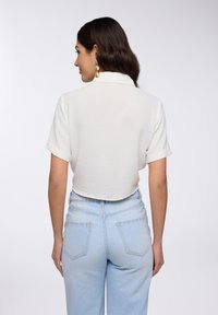 Top corto bianco e testurizzato con colletto, abbinato a jeans a vita alta blu chiaro con tasche posteriori e una vestibilità comoda.